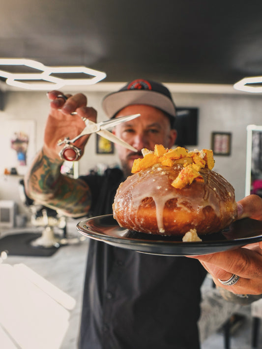 Lake City Deluxe barber holding a plate with a Lantern Donut collaboration called The Deluxe, a Peach Bourbon custard-filled donut.